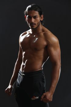 Muscular male model posing shirtless in a studio wearing sportswear. Dramatic lighting enhances physique.