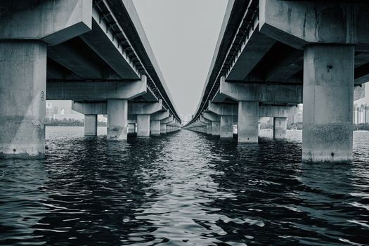 Black and white photograph of a symmetrical concrete bridge over a river in an urban setting., free online jigsaw puzzle on JigsawPuzzlesFreeOnline.org