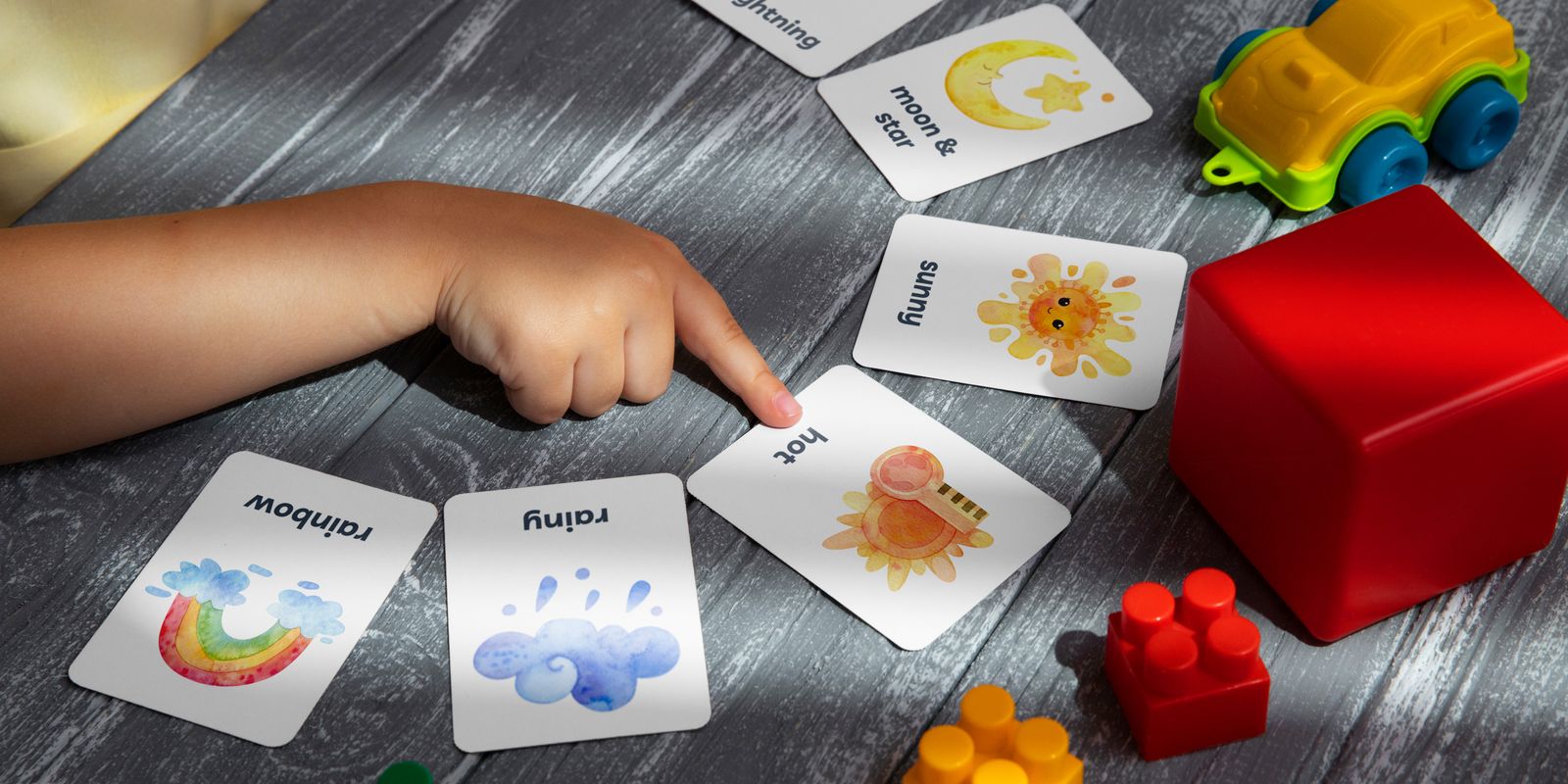 Close-up of a child pointing at colorful educational flashcards and toys, promoting learning and creativity.