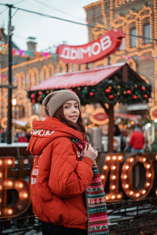 Free Joyful young woman in winter attire at a vibrant festive market with decorative lights. Stock Photo