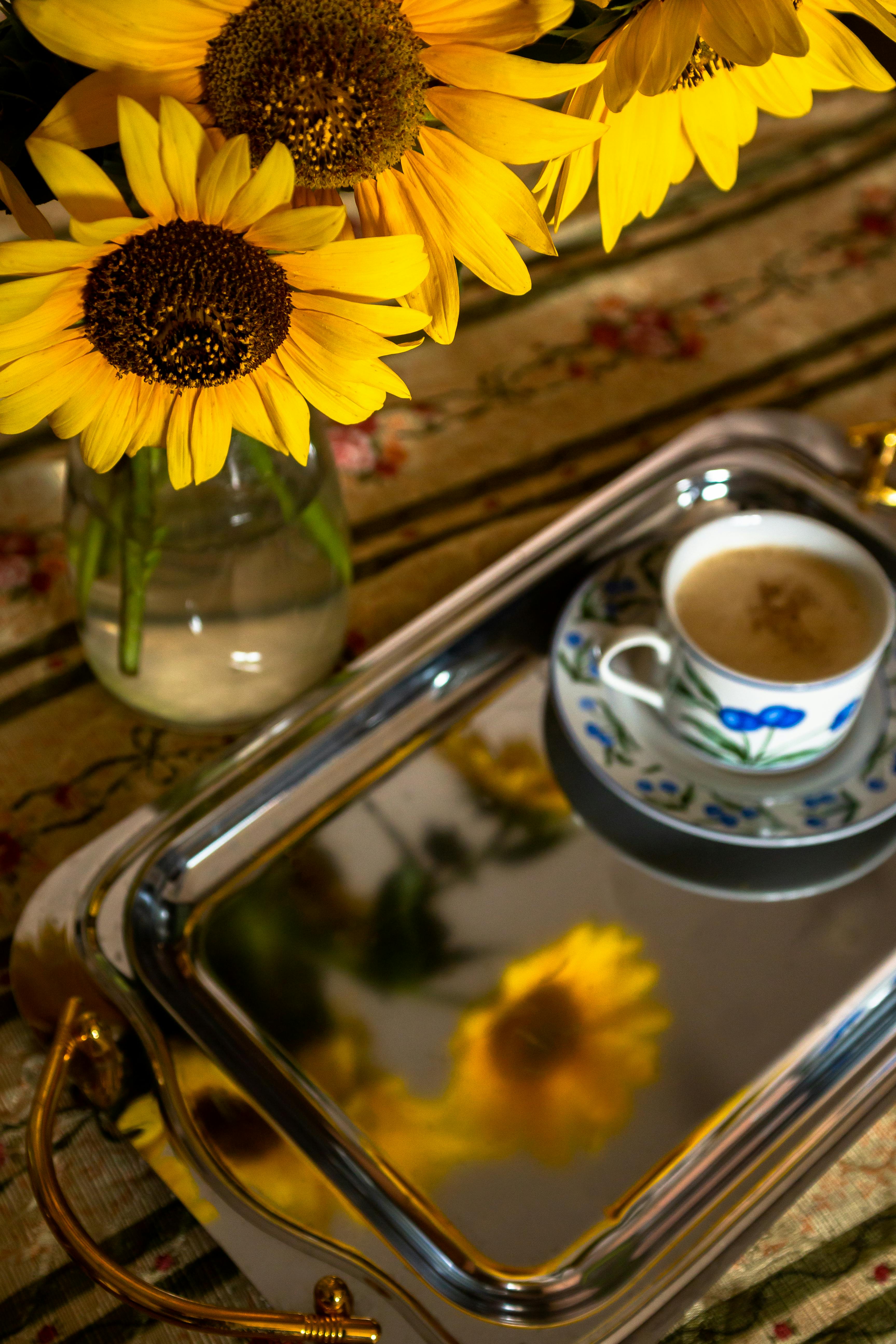 Vibrant sunflowers in vase and coffee on a reflective tray, creating a warm, inviting scene.