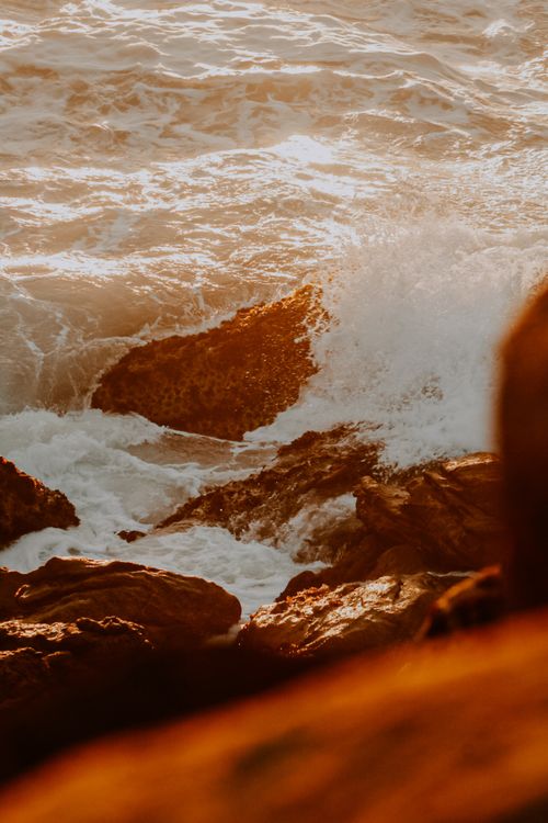 Free Capture of waves crashing against rocks, illuminated by a warm sunset glow on the rocky shoreline. Stock Photo