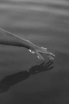 A serene black and white image of a hand reaching towards water with a reflection.