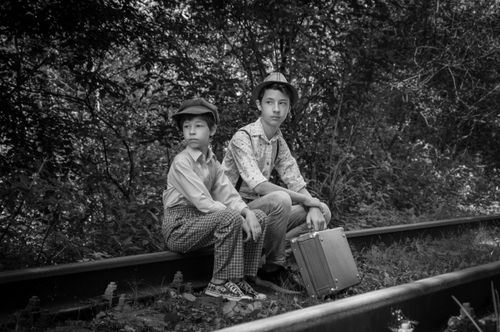 Free Two boys sitting on train tracks with a suitcase, embracing a vintage adventure theme. Stock Photo
