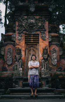 一名男子自信地站在一座装饰着复杂雕塑的巴厘岛华丽寺庙前