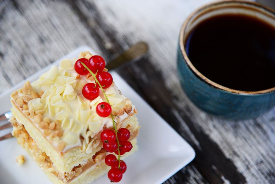 Delightful slice of cake with red currants and a hot cup of coffee, perfect for a sweet indulgence.