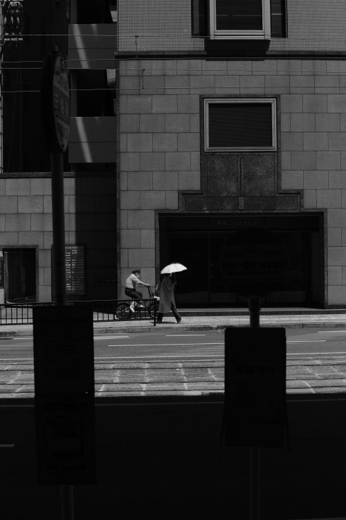 Free Monochrome city scene with a pedestrian holding an umbrella and a cyclist on an empty urban street. Stock Photo