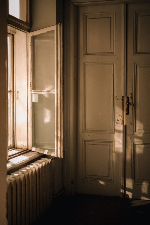 Free A serene interior scene with sunlight through an open window illuminating a classic door. Stock Photo