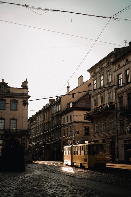 Historic city street scene with classic architecture and a yellow tram under power lines on a sunny day.