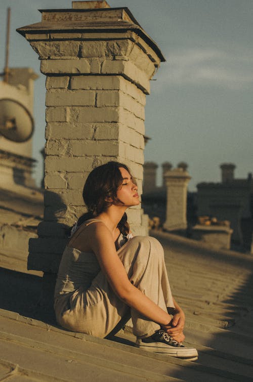 Young Woman Sitting on a Roof in Sunlight with Eyes Closed