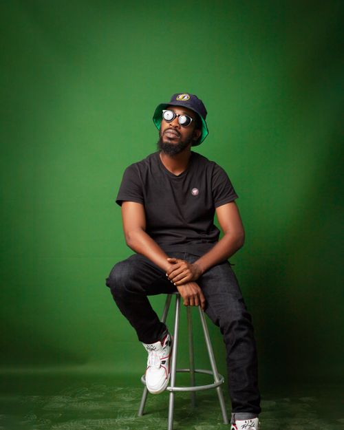 Free Fashionable man wearing black outfit and sunglasses, sitting in front of a green backdrop. Stock Photo