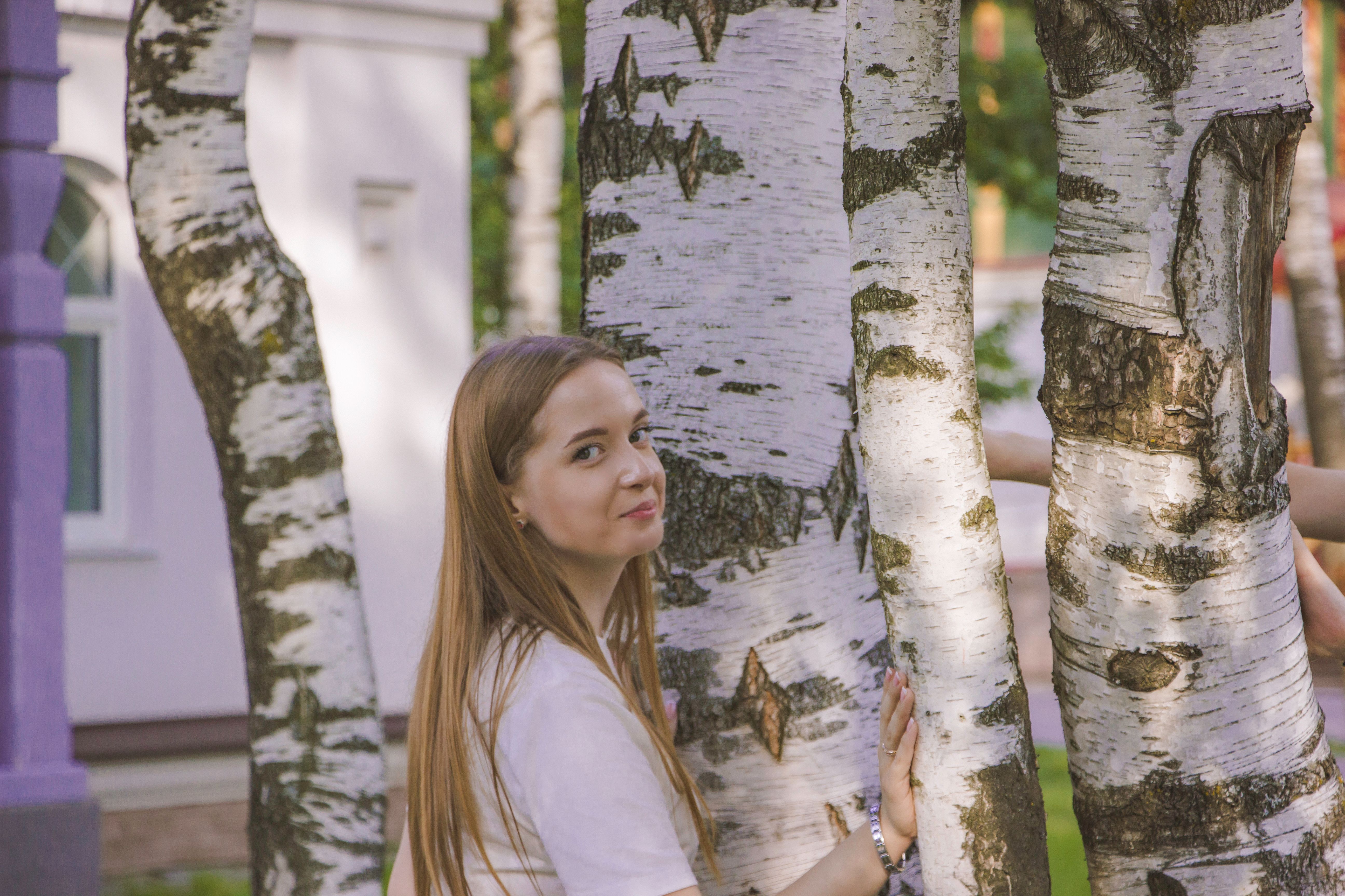 A young woman poses thoughtfully surrounded by birch trees.