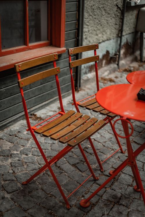 Free Cozy outdoor café scene featuring red metal chairs and table on cobblestone pavement. Stock Photo