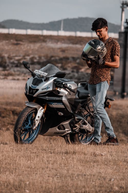 Free A young man stands beside a sporty motorcycle in a rural landscape, holding a helmet. Stock Photo