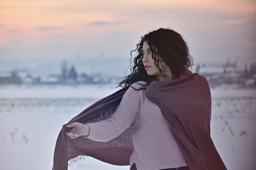 一位年轻女子裹着围巾，在白雪覆盖的原野上凝视着宁静的冬日日落