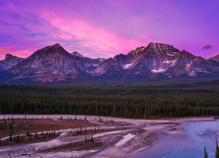 Breathtaking view of the Canadian Rockies at sunset with a vibrant purple sky.