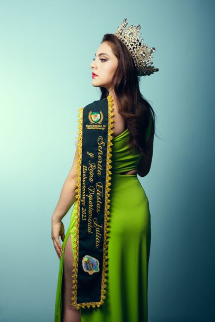 Elegant beauty pageant winner in a green dress with crown and sash on blue background.