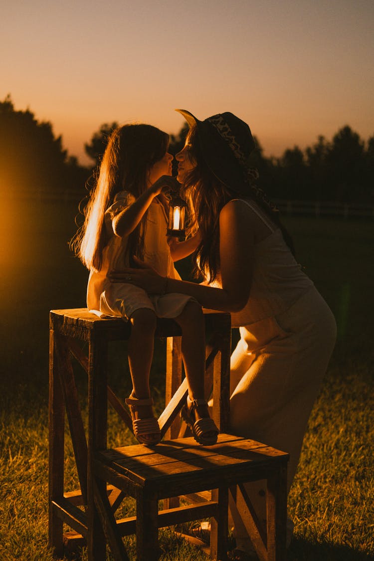 Woman With Her Daughter Standing Outside At Sunset 