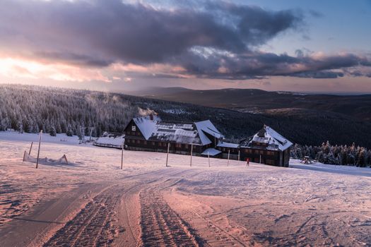 A scenic view of a snow-covered mountain lodge surrounded by winter forests at sunrise.