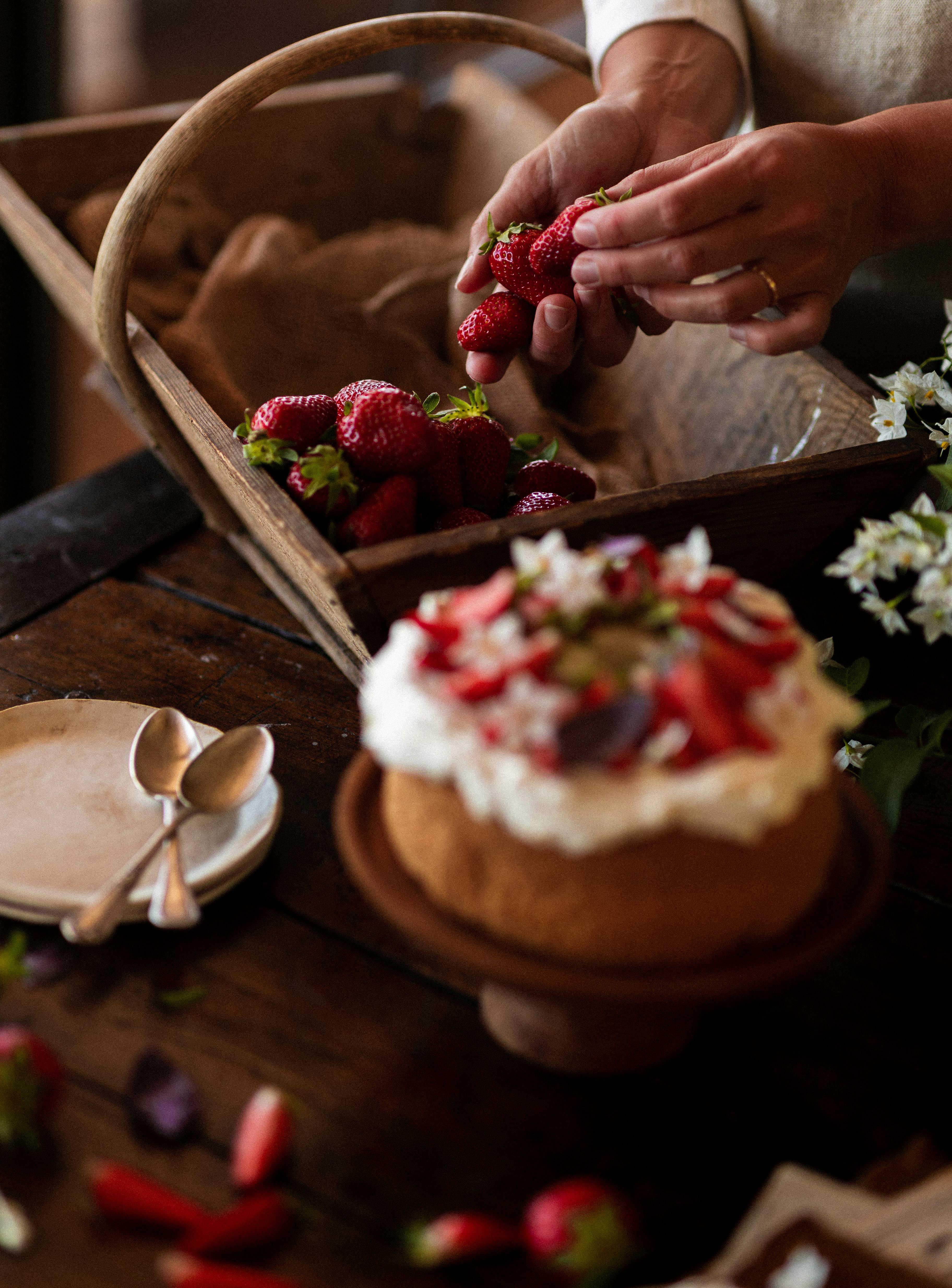 close up of woman putting strawberries in a basket standing next to a cake