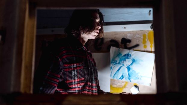 Moody portrait of a man near a graffiti wall and artistic painting at night.
