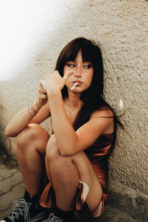 Brunette Woman with a Cigarette Sitting by a Wall