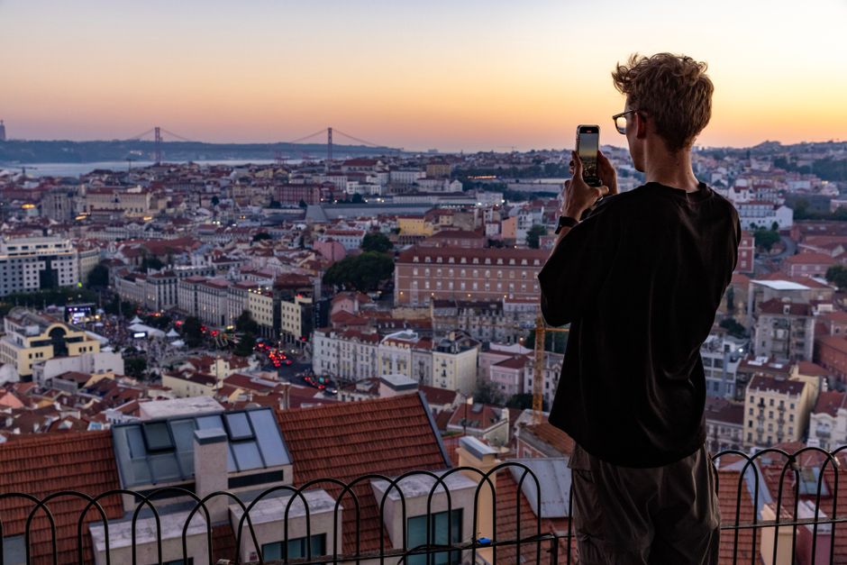 A man photographs the sunset over Lisbon, capturing its stunning cityscape from a high vantage point.