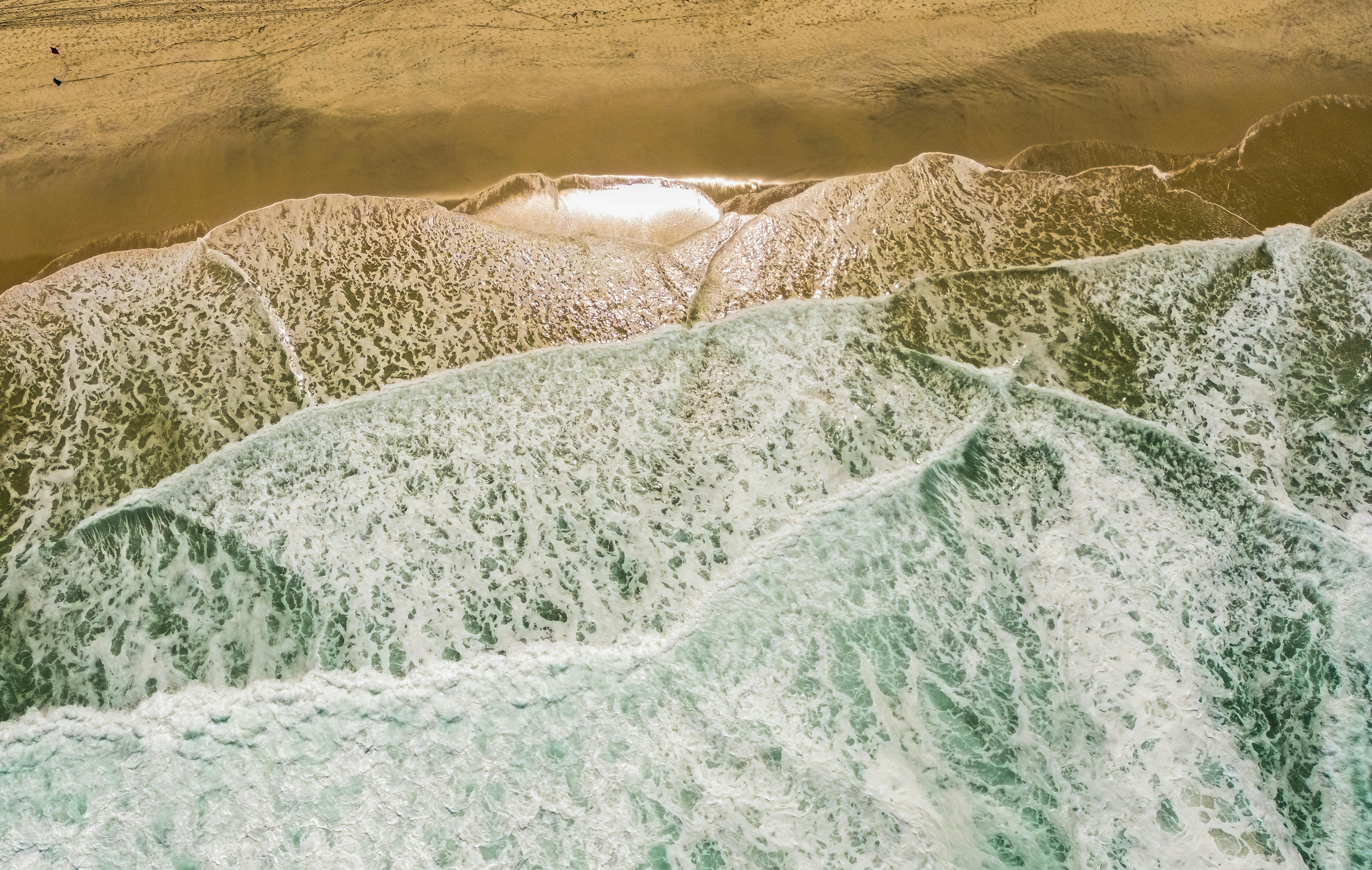 A stunning aerial shot capturing turquoise waves meeting the golden sands of Rio's Praia da Barra beach.