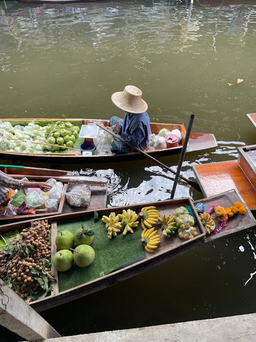Person in Hat Sitting with Fruit on Boats