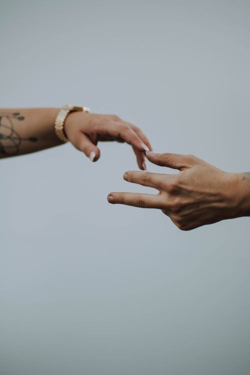 Free A touching moment depicted by two hands reaching out, featuring tattoos and a watch, set against a neutral background. Stock Photo