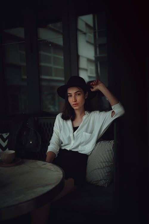 Woman in Hat and Shirt Sitting in Darkness in Room