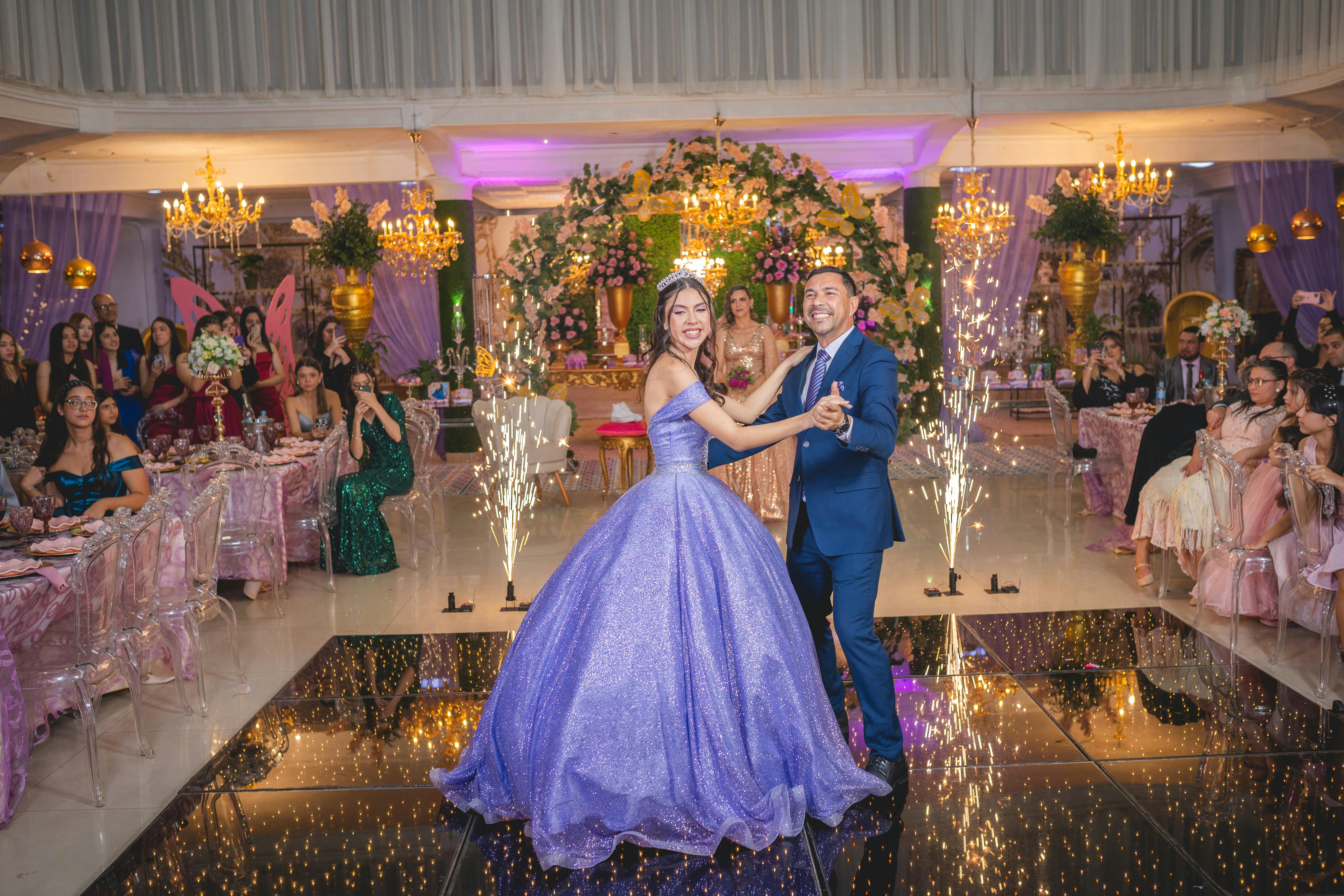 A bride and groom joyfully dance at a lavish wedding reception surrounded by guests and floral decor.