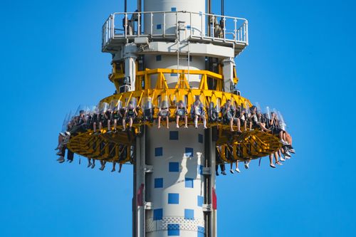 Free People enjoying a thrilling drop tower ride against a clear blue sky. Stock Photo
