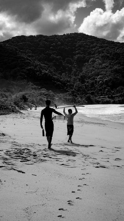 Black and White Photo of Men Walking with Surfboards on a Beach