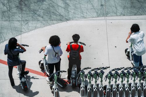 Free Group of young adults using electric scooters on a sunlit urban pavement. Stock Photo