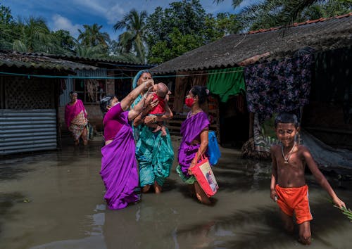 Women Wearing Traditional Clothing standing with Kids in a Flooded Village