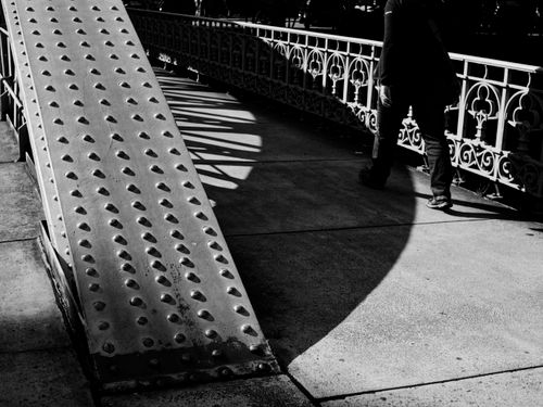 Free Artistic black and white photo of a person walking on a sunlit urban bridge. Stock Photo