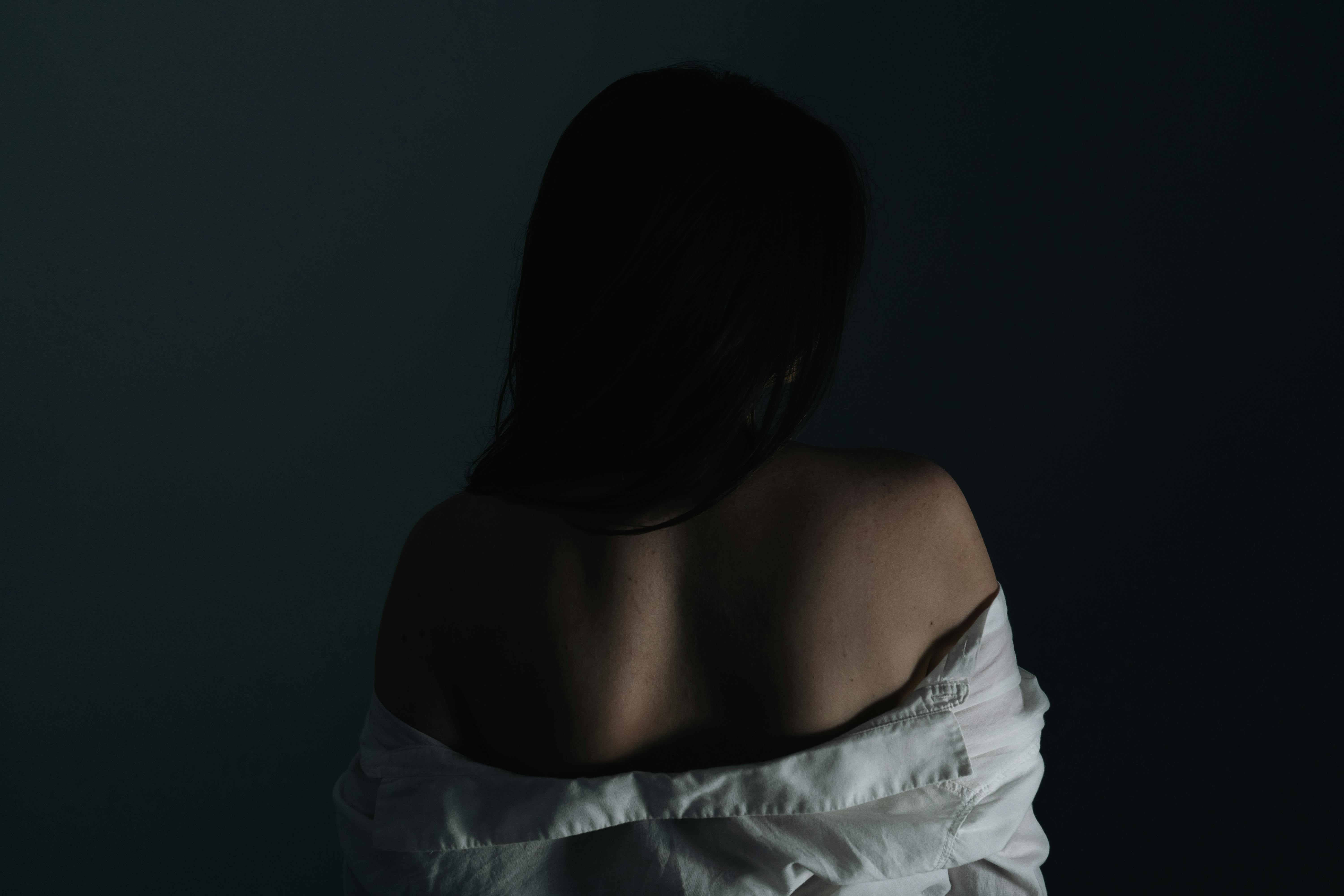An artistic depiction of a woman from behind, draped in shadow.