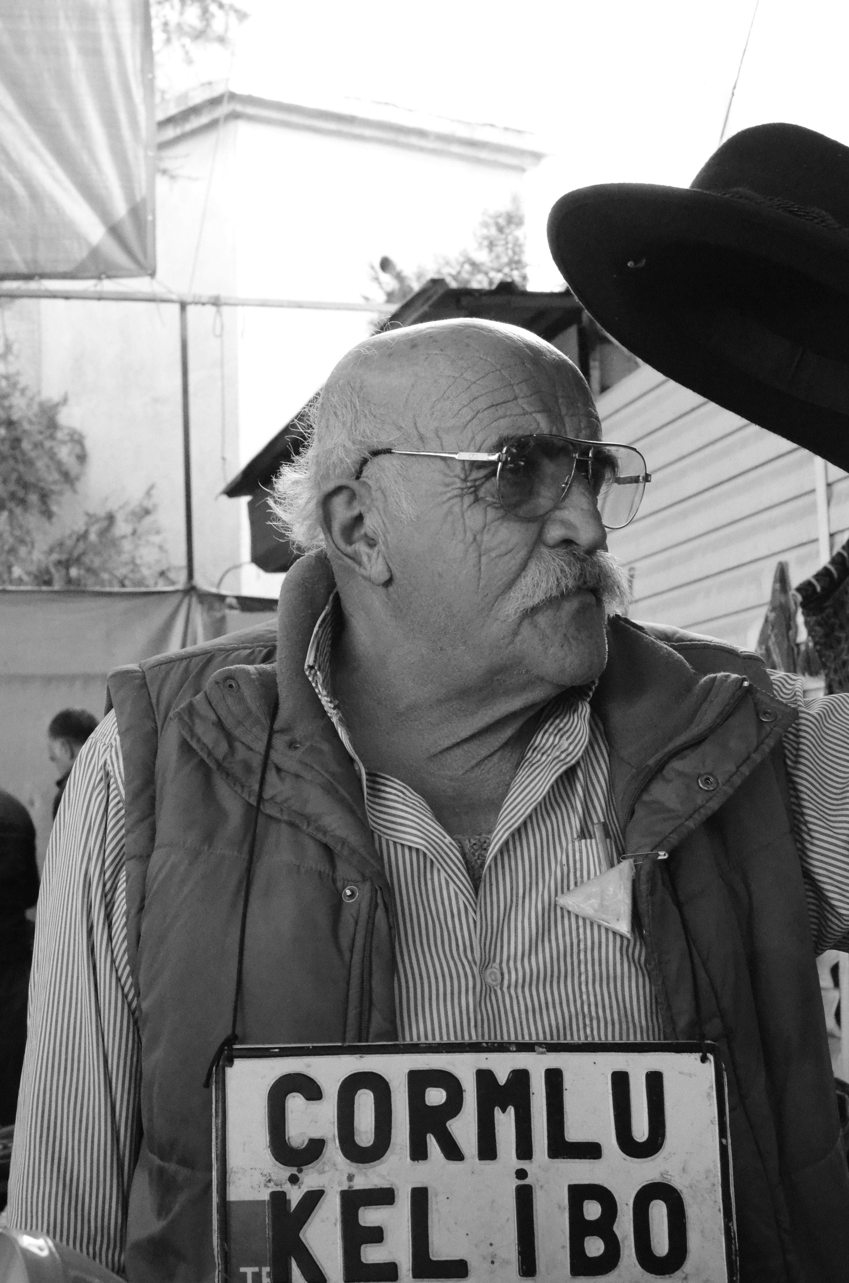 Striking black and white image of an elderly man with a hat and sign, outdoors.