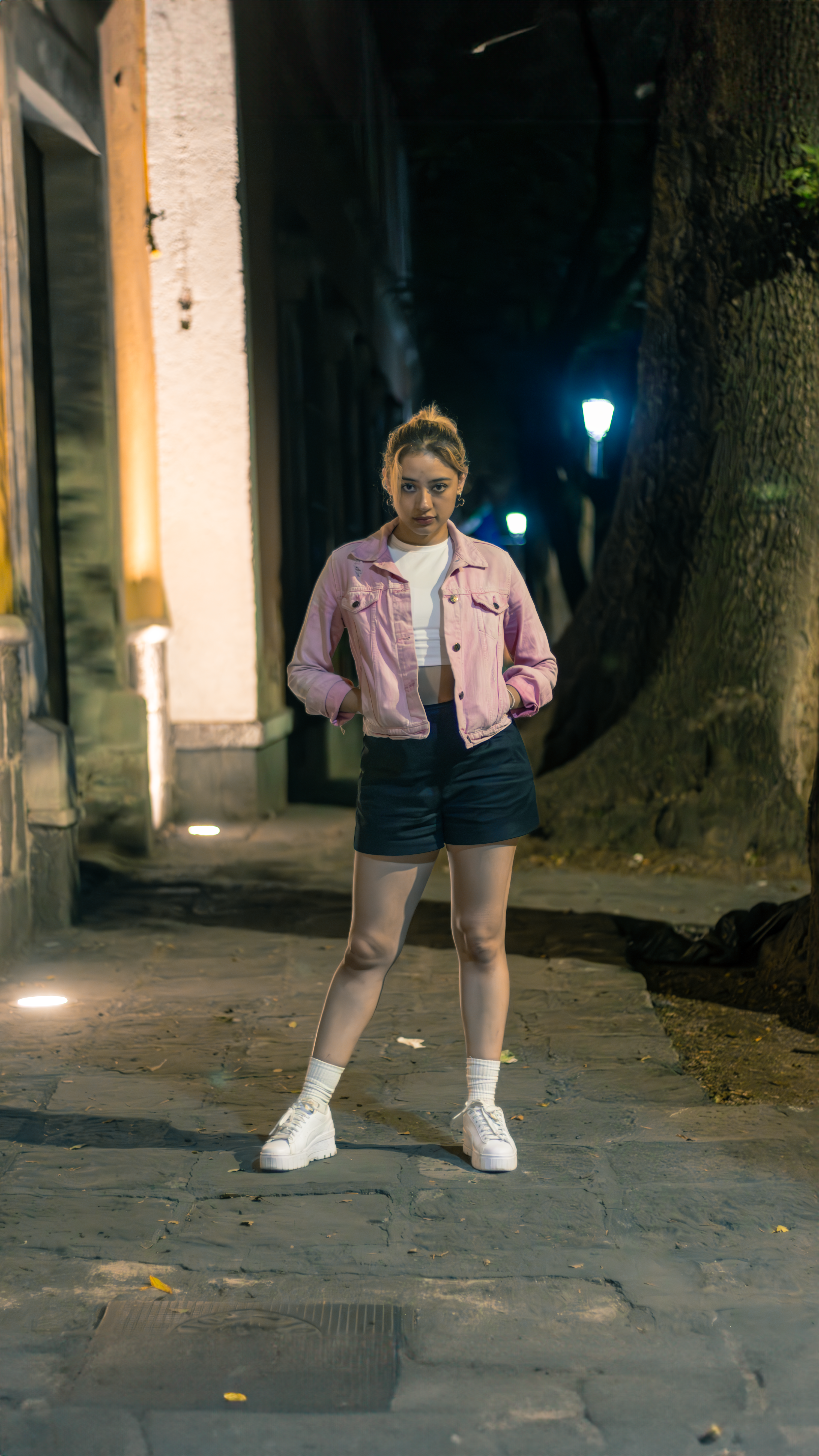 Fashion-forward woman in a pink jacket poses confidently on urban street at night.
