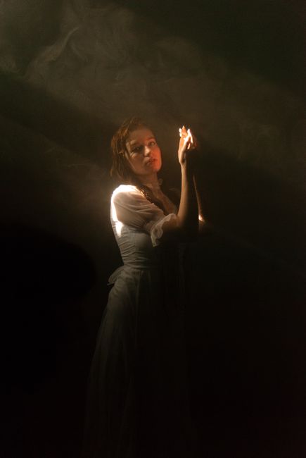 Elegant woman in white dress posing in dramatic lighting creating moody atmosphere.