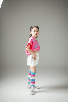 A young girl in a vibrant outfit poses confidently in a studio setting.