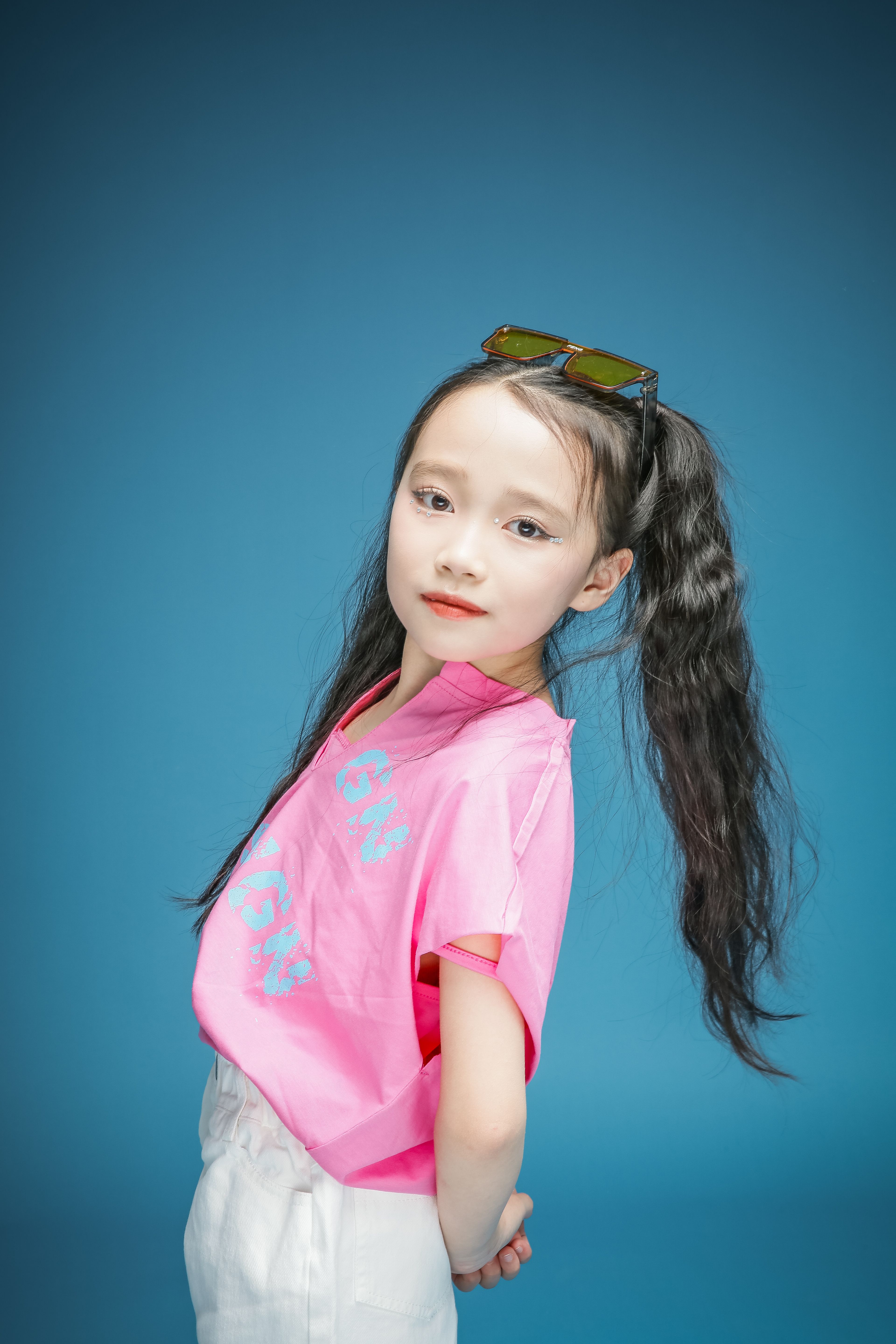 Fashionable young girl with long hair in pink t-shirt against a blue background.