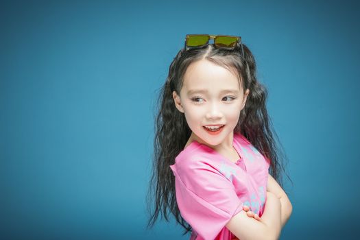 Happy young girl with long black hair posing confidently against a blue backdrop.