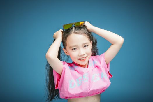 Energetic studio portrait of a young girl in colorful clothing holding sunglasses.