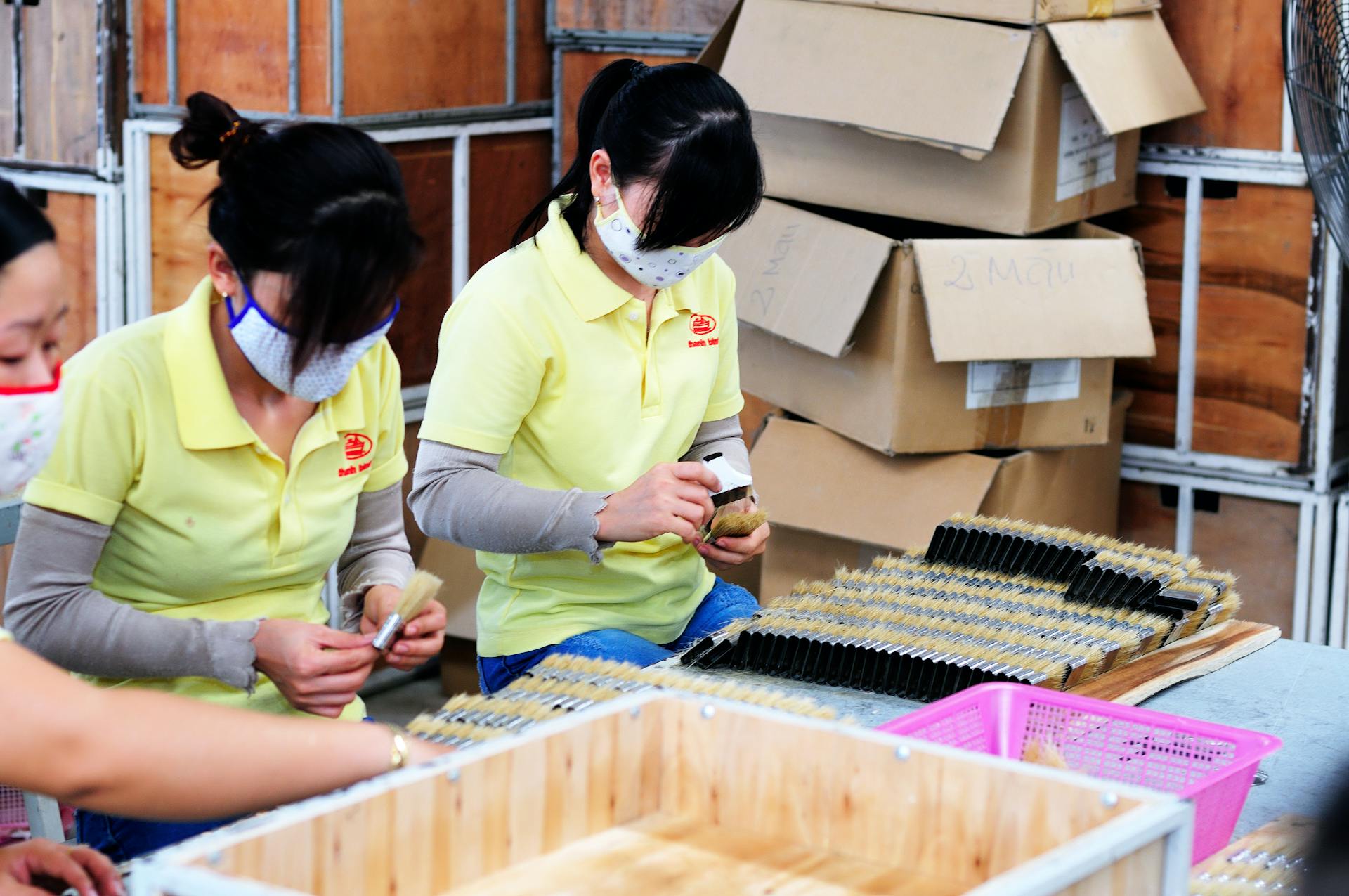 A group of women working in a factory, engaged in product assembly, wearing face masks for safety.