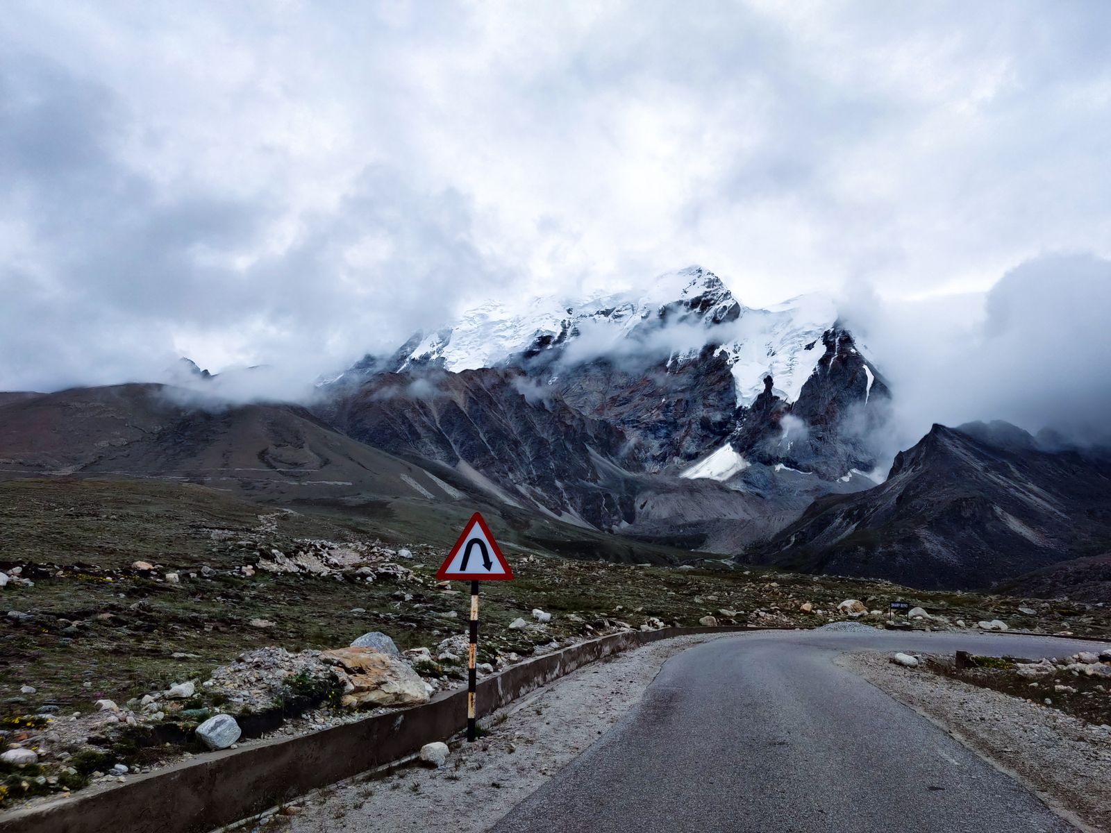 A mountain road above the treeline in North Sikkim running towards snow covered peaks wrapped in cloud