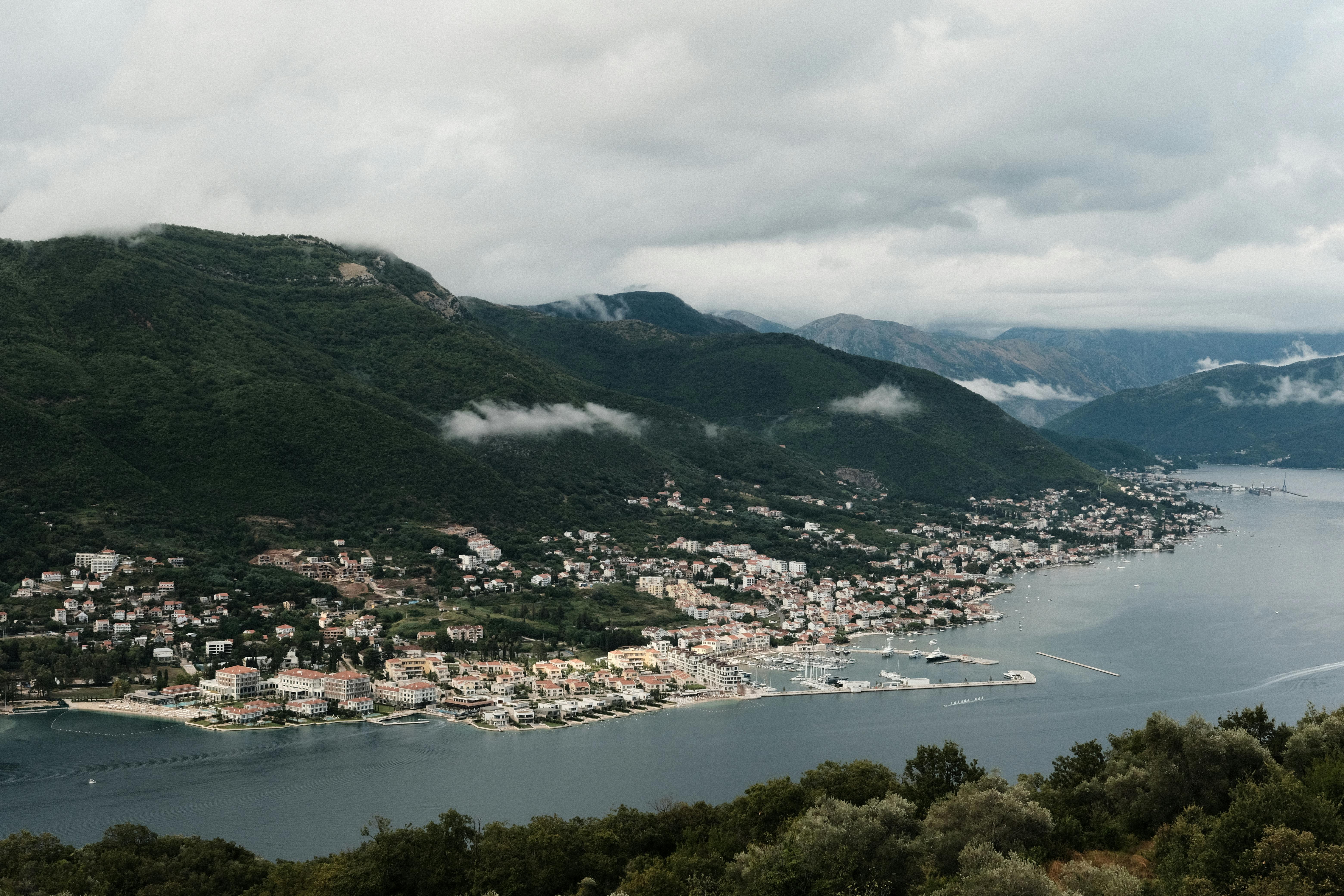 A breathtaking view of a coastal town and lush mountains in Montenegro with dramatic cloud formations.
