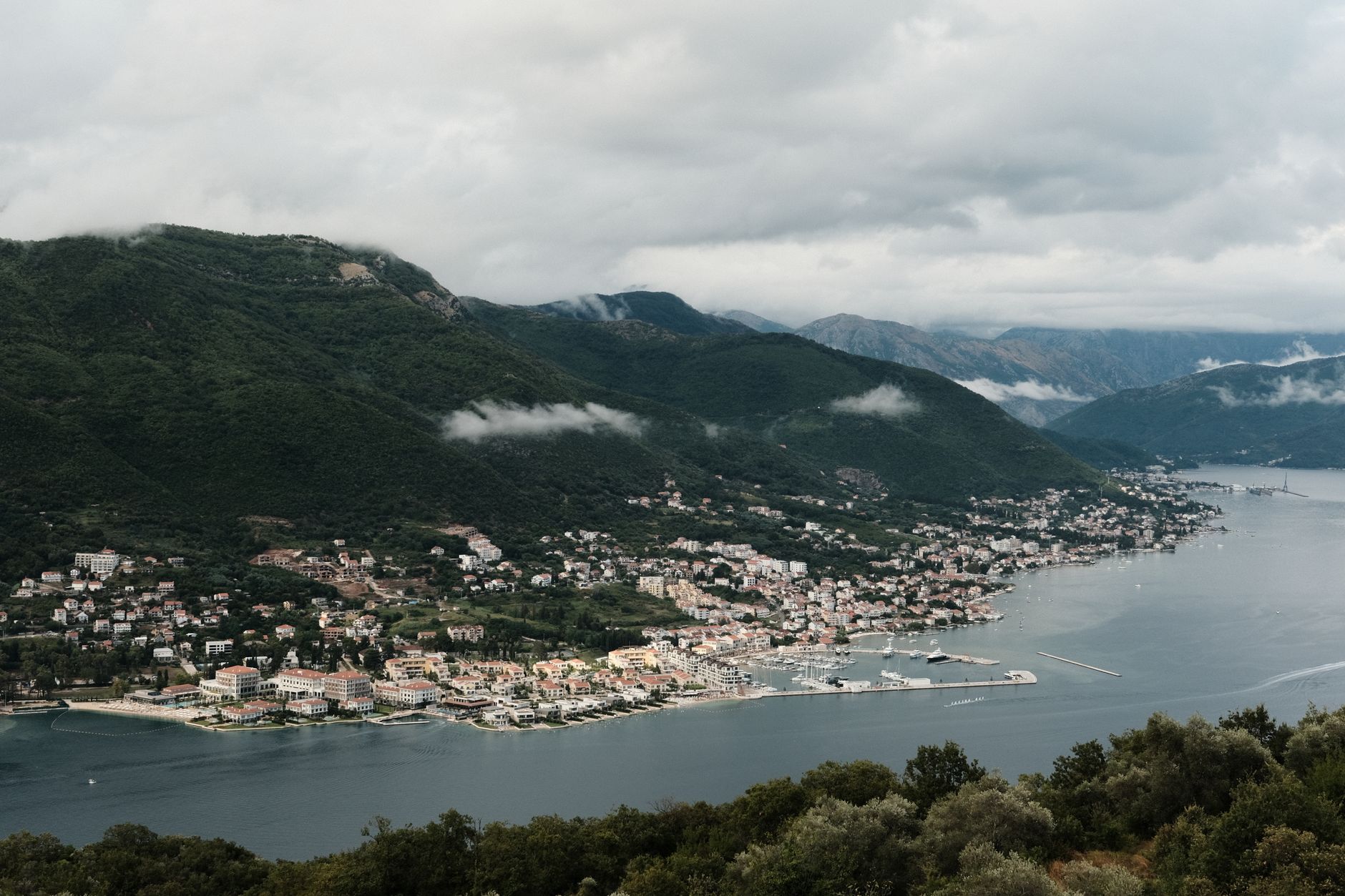 A breathtaking view of a coastal town and lush mountains in Montenegro with dramatic cloud formations.