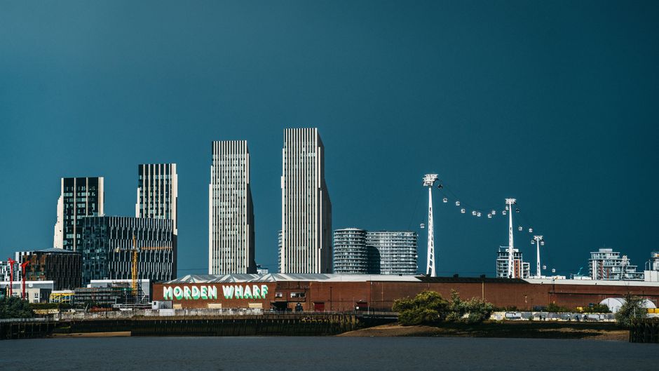 View of London skyline featuring modern skyscrapers and the Morden Wharf area by the river.